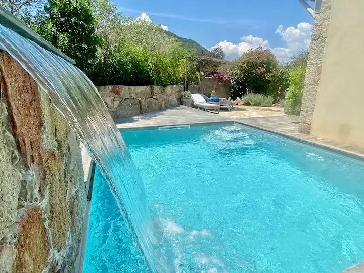 Piscine chauffée avec cascade d'eau et murs en pierre traditionnelle dans une villa de luxe à Porto-Vecchio.