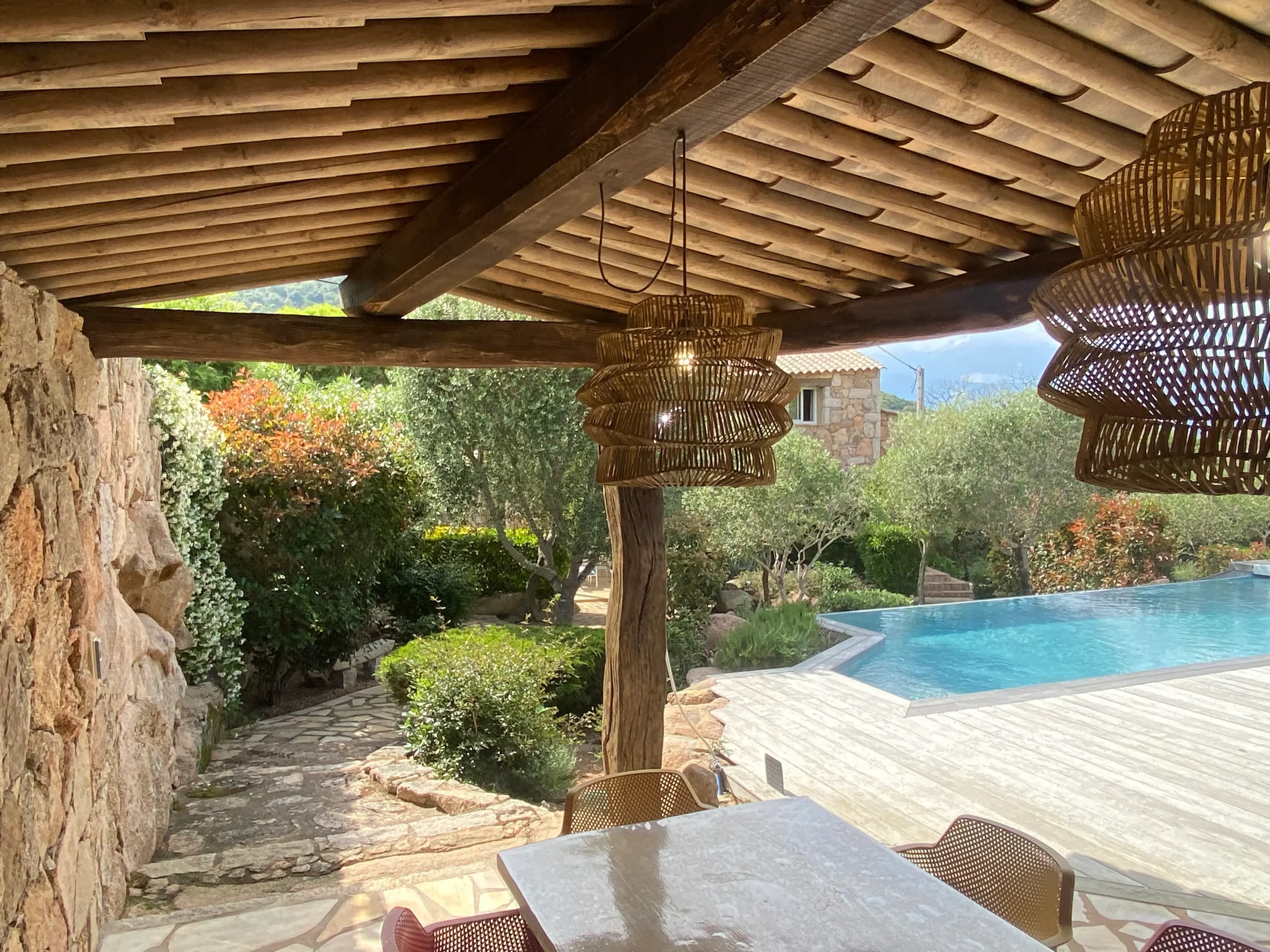 Terrasse couverte en bois avec luminaires design et vue sur la piscine à débordement d'une location villa de luxe à Porto-Vecchio.
